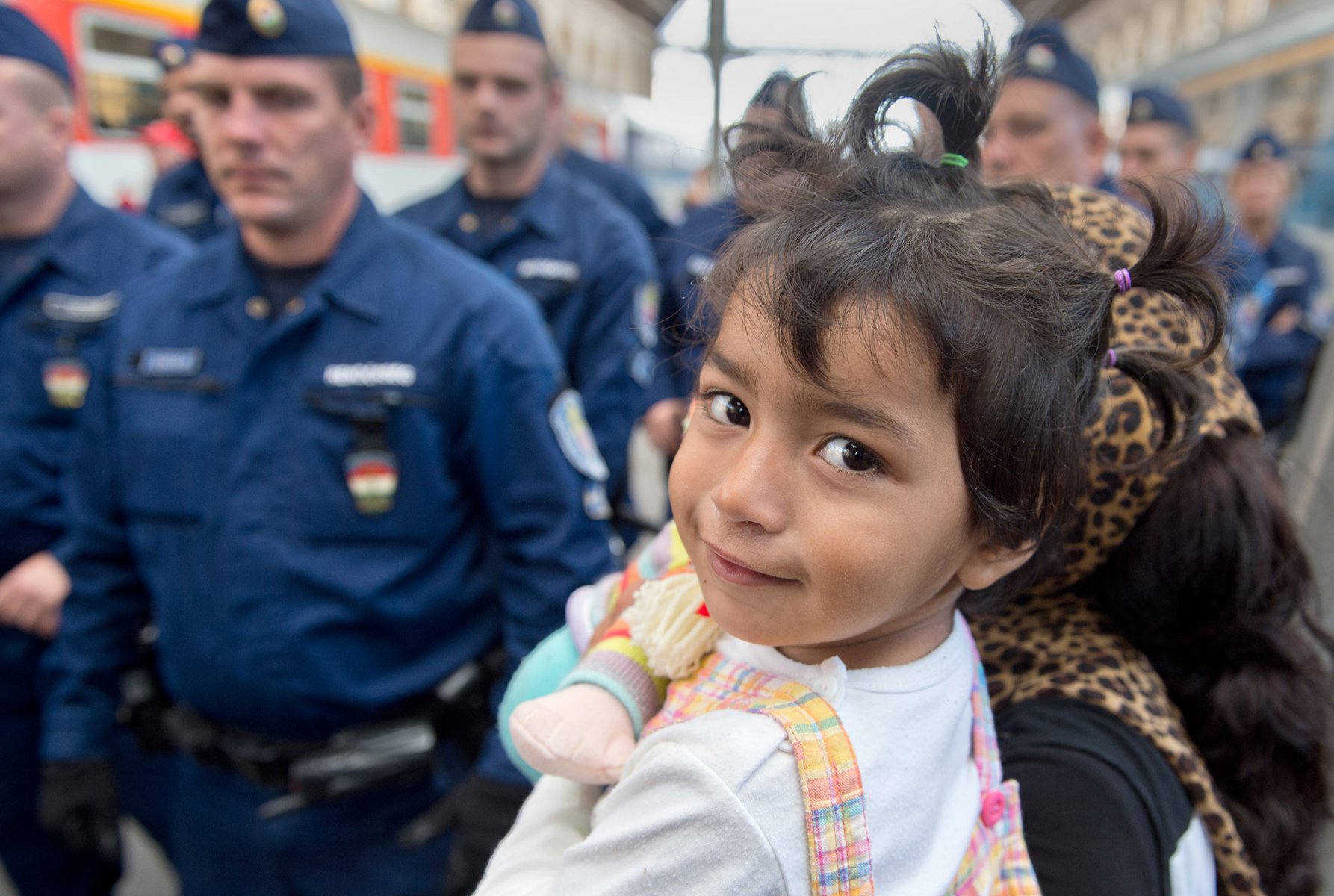 Die kleine Chuschi aus Masar I-Scharif will  am 06.09.2015 im Ostbahnhof in Budapest, Ungarn auf dem Arm ihrer Mutter zu einem Zug nach Österreich gelangen als Polizisten den Bahnsteig kurzfristig wegen Überfüllung sperren. Foto: Boris Roessler/dpa